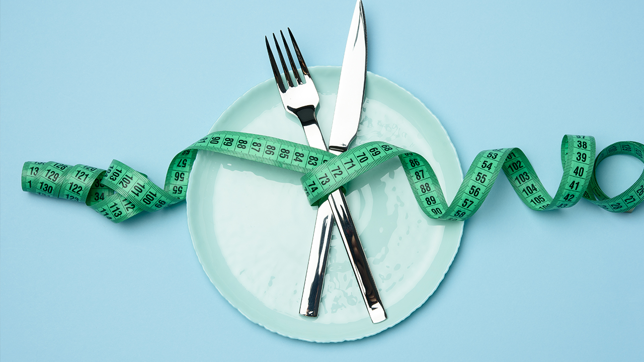 silver knife and fork on a light blue plate wrapped in a tape measure on a light blue background