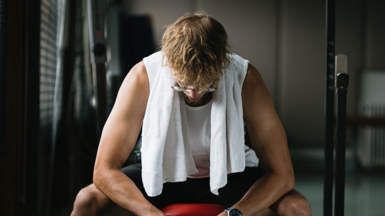 man sitting down in white vest with white towel around neck looking at the floor